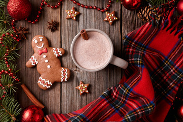 Cup of hot chocolate or cocoa with gingerbread man, stars cookies and warm scarf composition in fir tree decorations frame on vintage wooden table background. Homemade traditional food recipe.