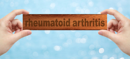 Hands holding a wood engrave with word rheumatoid arthritis