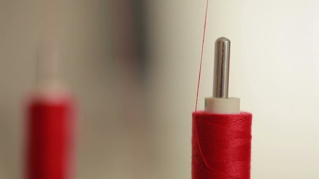Sewing bobbin being wound up on a sewing machine with red thread. Machine in clothing industry production. Close up.