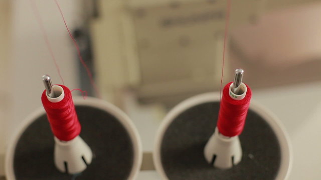 Sewing bobbin being wound up on a sewing machine with red thread. Machine in clothing industry production. Close up.
