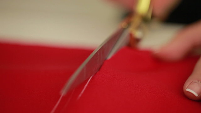 Slow motion of woman hands with scissors cutting red fabric on a tabletop. Designer scissor cloth. 