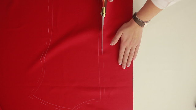 Slow motion of woman hands with scissors cutting red fabric on a tabletop. Designer scissor cloth. 