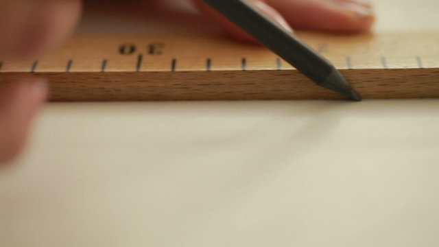 Fashion designer working on table. Hand of female tailor drawing pattern at paper in her studio. Young female tailor with measuring tape on shoulders working in workshop.