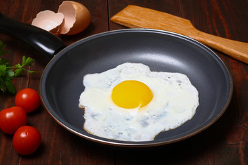 Pan of fried egg, with cherry-tomatoes and parsley on a wooden table surface