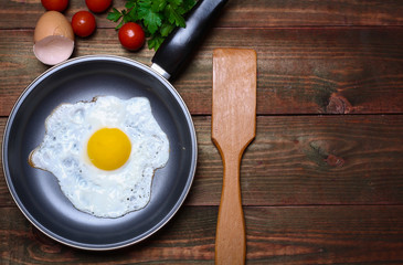 Pan of fried egg, with cherry-tomatoes and parsley on a wooden table surface
