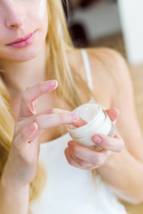 Beautiful young woman spreading cream on her face.