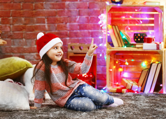 Pretty little girl in red hat sitting in Christmas decorated room