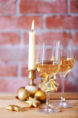 Two glasses of wine with candle and Christmas toys on wall background