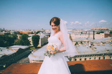 Fototapeta na wymiar Happy bride with a wedding bouquet on the roof of the city