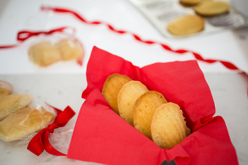 Madeleines in a red napkin on a white marble pastry board amid gift-wrapped sweets.