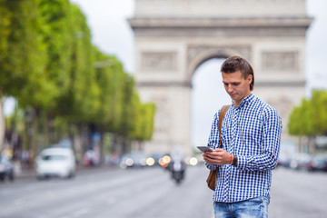 Fototapeta premium Young caucasian man holding a phone on the Champs Elysees in Paris