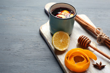 Mulled wine in a mug with citruses on board against grey wooden background, close up