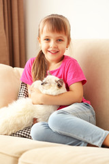 Little cute girl with kitten on sofa at home