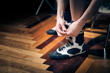 Closeup of young boxer's hands tying trainers on parquet background