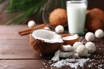 Candies in coconut flakes, glass of milk and fresh coconut on dark wooden background