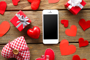 Smart phone with blank screen and hearts on old wooden table