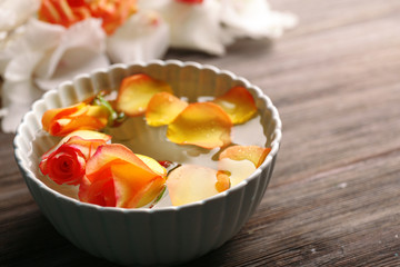 Beautiful orange rose and petals in a bowl of water on wooden background