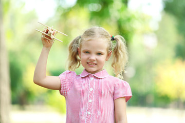 Blonde little girl plays with wooden plane at the park