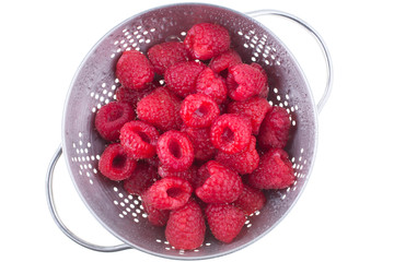 Raspberries in a metal colander on a white translucent table, lit from above and below.