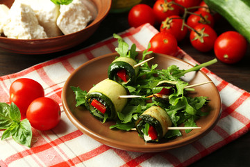 Zucchini rolls with cheese, bell peppers and arugula on plate, close-up, on table background