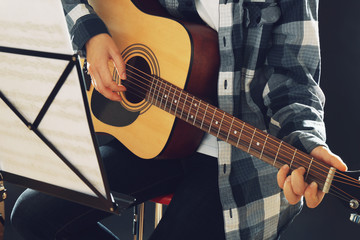 Fototapeta premium Musician plays guitar on black background in studio with musical notes holder, close up