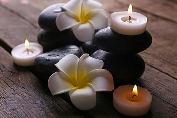 Relaxing composition with exotic fragipani flower, pebbles and candles on wooden background
