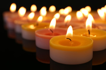 Many burning small candles on dark background, close-up