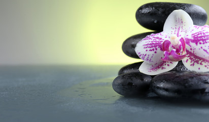Black pebbles with orchid on grey table, close up