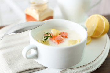 Delicious salmon cream soup with sliced lemon on white tray, close up