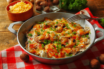 Roasted mushrooms, chicken and cheese gratin in pan, on wooden background