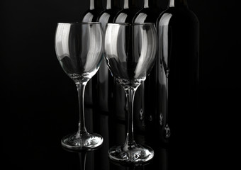 Glasses and wine bottles in a row on black  background, close up