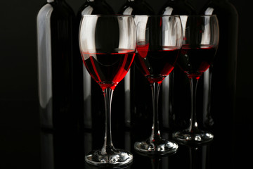 Wine glasses against bottles in a row on black background, close up