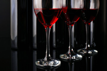 Wine glasses against bottles in a row on black background, close up