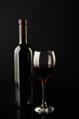 Red wine glass and bottle on black background, close up