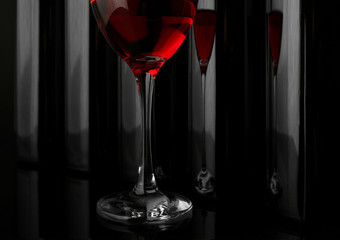 Red wine glass against bottles in a row on black background, close up