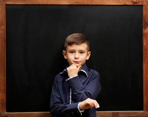 Cute boy posing at the clean blackboard, in the classroom