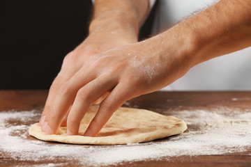 Hands preparing dough basis for pizza on the wooden table, close-up