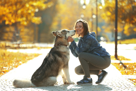 Happy Young Woman Walking With Her Dog In Park