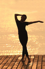 Silhouette young woman practicing yoga on the beach at sunset.