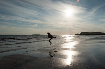 a man gives a kick while jumping on the beach at sunrise