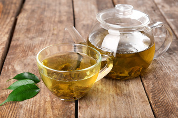 Glass cup of tea and teapot on wooden background