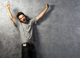 Young man listening music with headphones on grey wall background