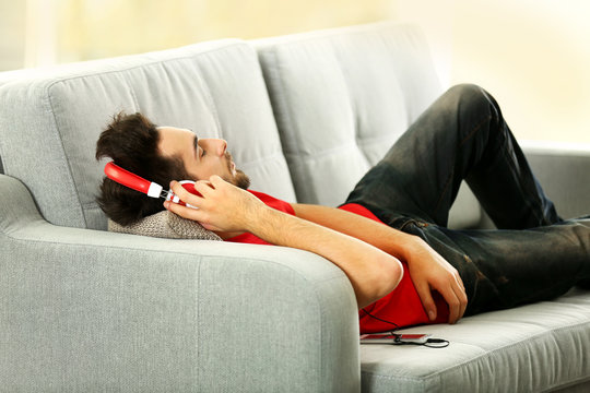 Handsome man listens music with headphones on grey sofa in the room