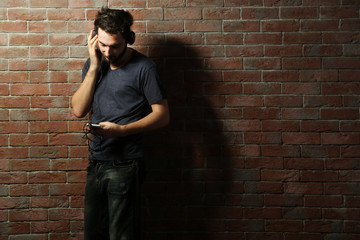 Young handsome man listening music with headphones on brick wall background