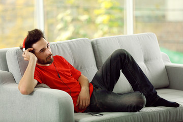 Handsome man listens music with headphones on grey sofa in the room