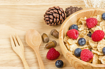 Bowl of cereals with raspberries and blueberrys on a wooden table.