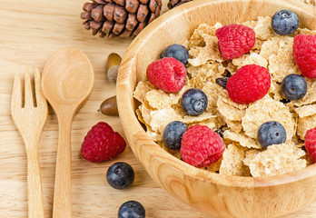 Bowl of cereals with raspberries and blueberrys on a wooden table.