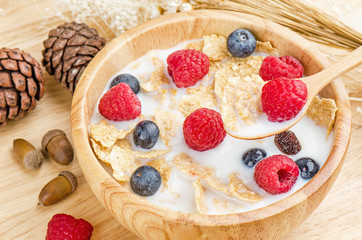 Bowl of cereals with raspberries and blueberrys on a wooden table.