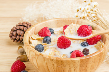Bowl of cereals with raspberries and blueberrys on a wooden table.