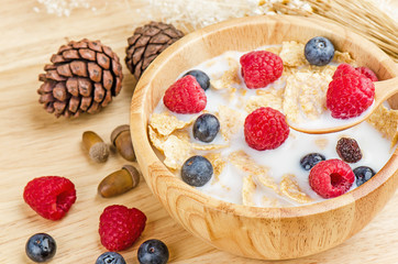 Bowl of cereals with raspberries and blueberrys on a wooden table.
